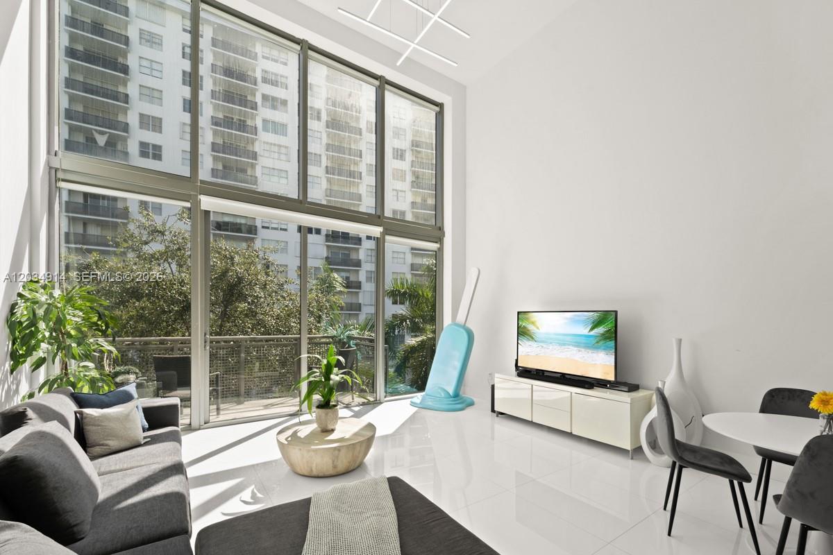 A modern living room features floor-to-ceiling windows, white tile floors, and a large television — 6000 Collins Ave # 517, Miami Beach FL 33140, MIAMI BEACH, FL