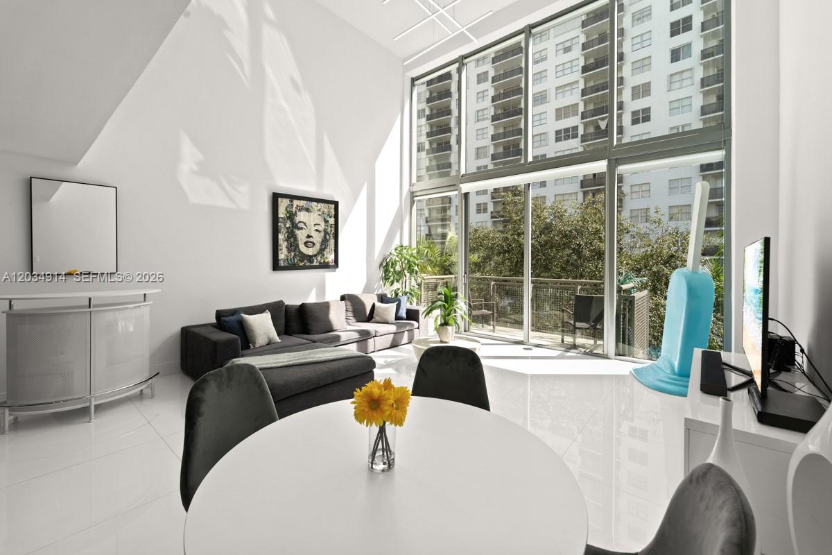 A bright living and dining area features floor-to-ceiling windows, white tile floors, and high ceilings — 6000 Collins Ave # 517, Miami Beach FL 33140, MIAMI BEACH, FL