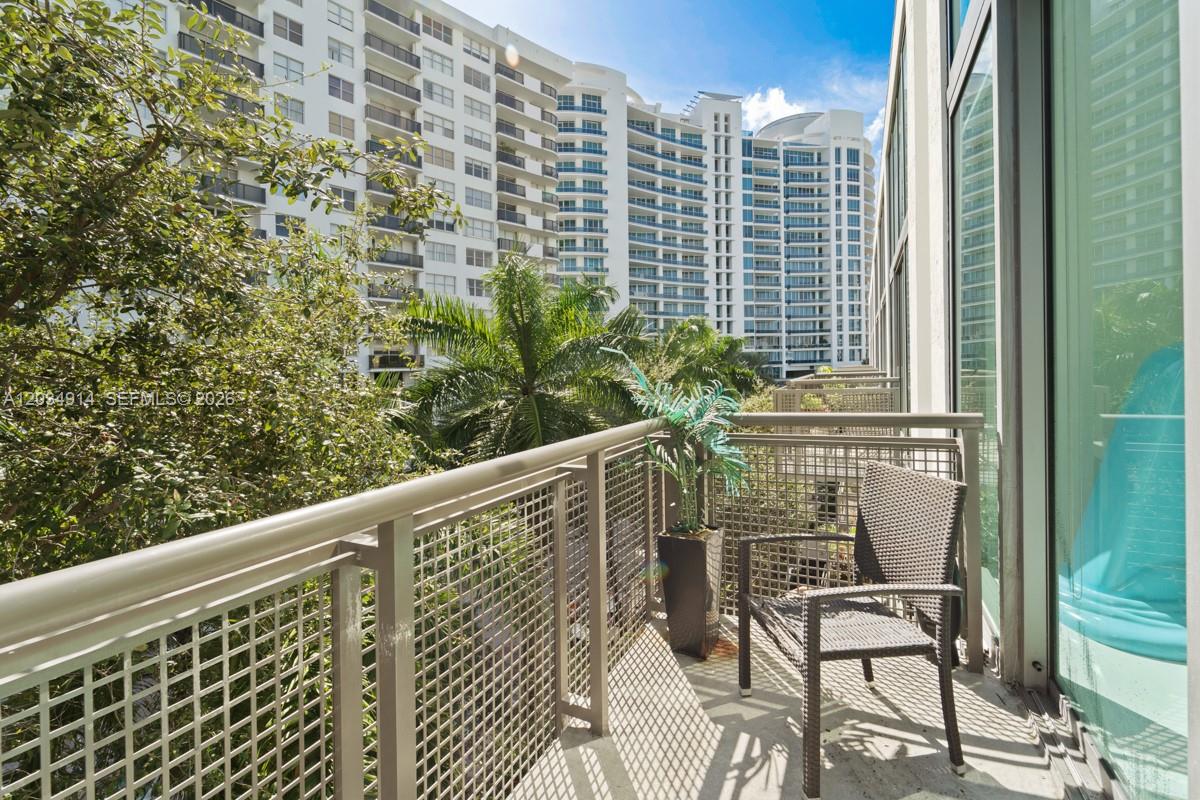 A balcony with a metal railing, a single chair, and a potted plant overlooks trees — 6000 Collins Ave # 517, Miami Beach FL 33140, MIAMI BEACH, FL