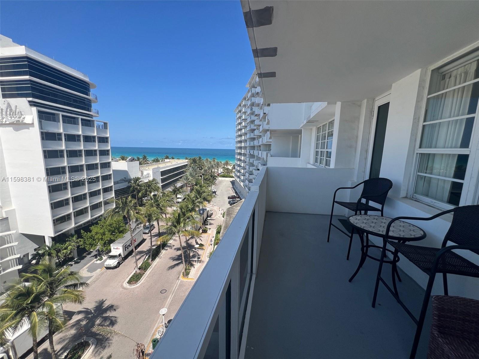 A balcony with a small table and two chairs overlooks a street and the ocean — 100 Lincoln Rd # 808, Miami Beach FL 33139, MIAMI BEACH, FL