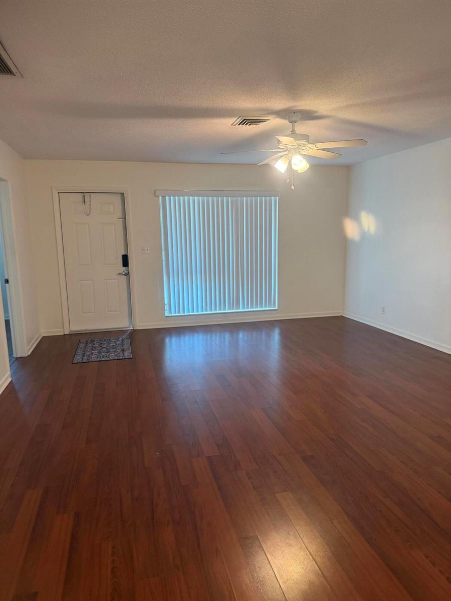 An empty living room features wood-look flooring, a ceiling fan, and a white front door — 1151 NE 26th Avenue, Pompano Beach FL 33062, POMPANO BEACH, FL