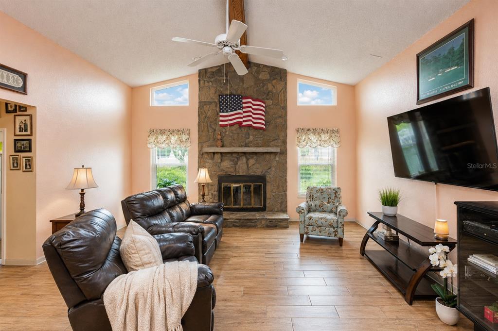 A living room features a stone fireplace, vaulted ceiling, wood-look tile flooring, and leather furniture — 7438 GATES CIRCLE, SPRING HILL, FL