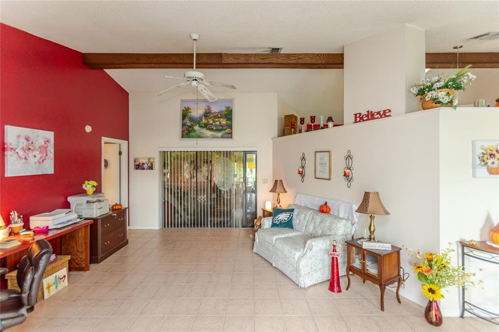 A living room features a red accent wall, tile flooring, a ceiling fan, and furniture — 7438 GATES CIRCLE, SPRING HILL, FL