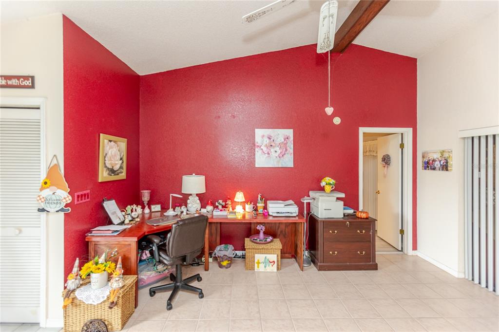 A home office features a red accent wall, a wooden corner desk, and tile flooring — 7438 GATES CIRCLE, SPRING HILL, FL
