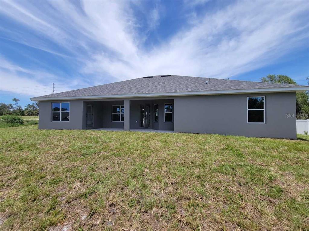 The rear exterior of a gray stucco house features a covered patio and multiple windows — 4626 SW 103RD STREET ROAD, OCALA, FL
