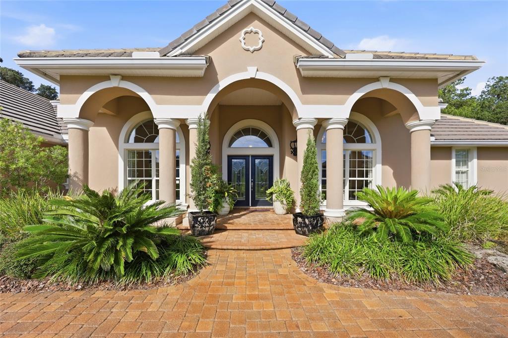 A tan house exterior features a paved walkway leading to a columned entryway with double doors — 5 ROMA COURT, PALM COAST, FL