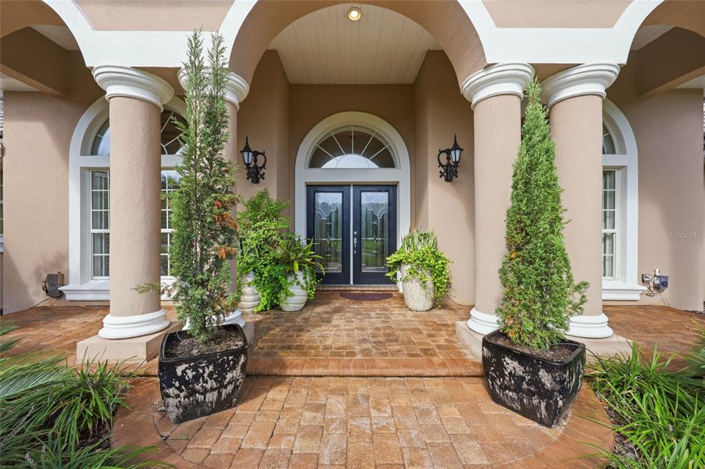A front entryway features double doors, arched windows, and two large planters with tall shrubs — 5 ROMA COURT, PALM COAST, FL
