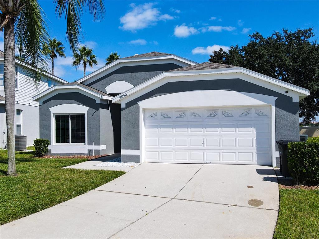 A gray single-story house with a white garage door and a concrete driveway — 8050 KING PALM CIRCLE, KISSIMMEE, FL