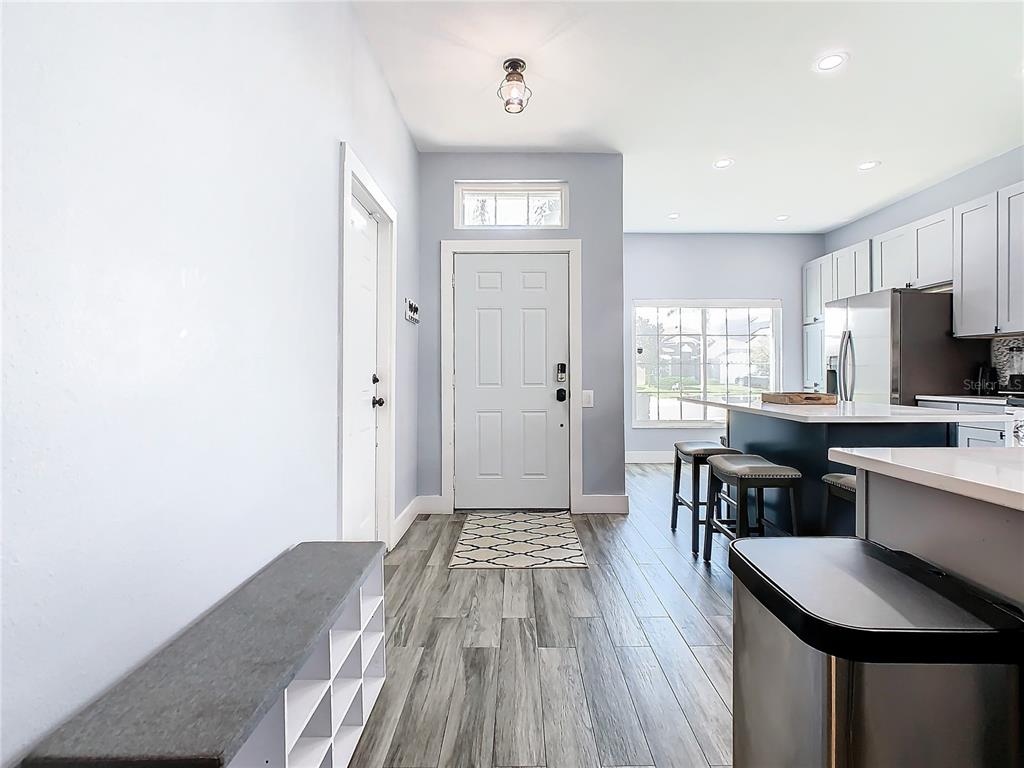 An entryway with wood-look flooring leads into an open-concept kitchen with a breakfast bar — 8050 KING PALM CIRCLE, KISSIMMEE, FL