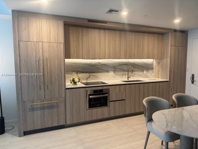 A modern kitchen features wood-grain cabinetry, a marble backsplash, and integrated appliances — 77 SE 5th St # 312, Miami FL 33131, MIAMI, FL