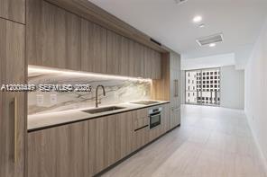 A modern kitchen features wood-grain cabinetry, a marble backsplash, and stainless steel appliances — 77 SE 5th St # 312, Miami FL 33131, MIAMI, FL