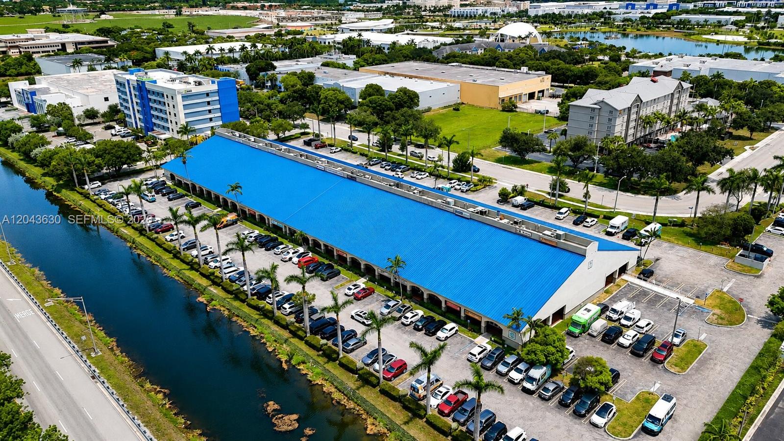 An aerial view shows a long commercial building with a blue roof beside a canal — 8726 NW 26 ST # 18, Doral FL 33172, DORAL, FL