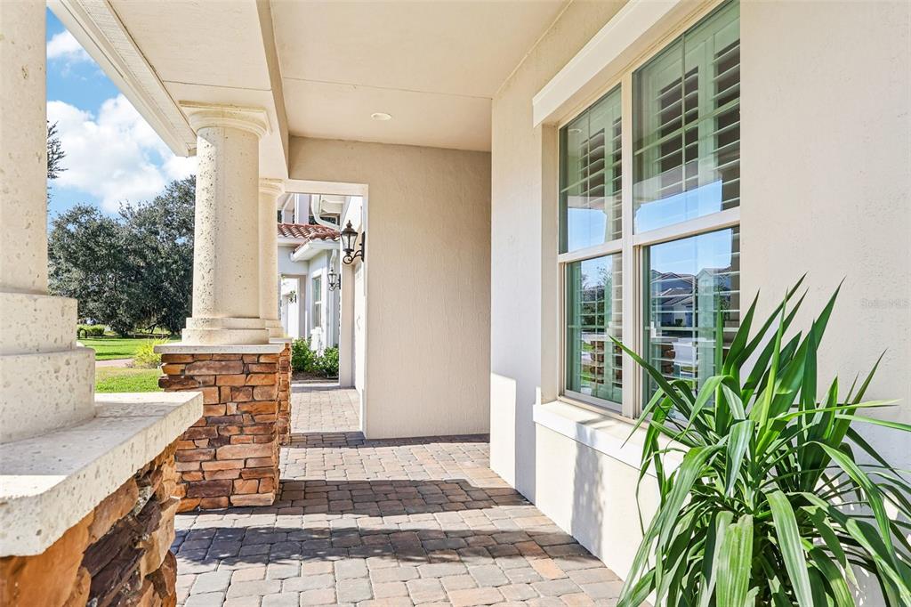 A covered stone-columned porch with paver flooring leads to a doorway and a large window — 13265 BROMBOROUGH DRIVE, ORLANDO, FL