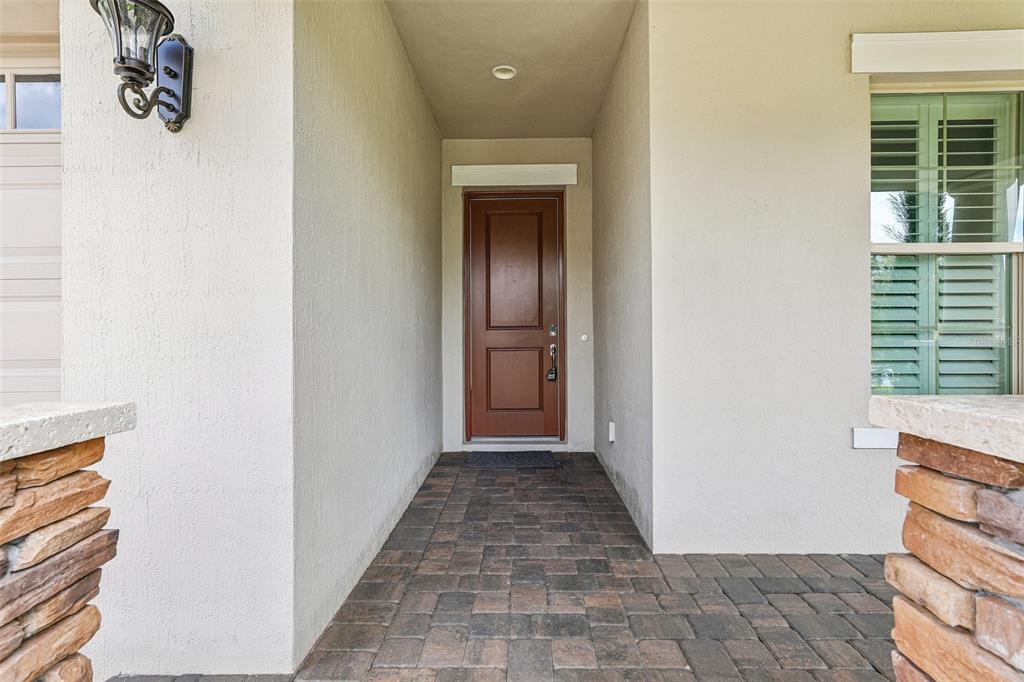 A brown front door is centered in a covered entryway with stone pillars and pavers — 13265 BROMBOROUGH DRIVE, ORLANDO, FL