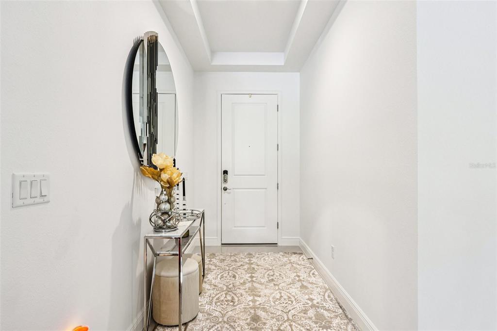 A bright entryway features a white door, a console table, a round mirror, and patterned rug — 13265 BROMBOROUGH DRIVE, ORLANDO, FL