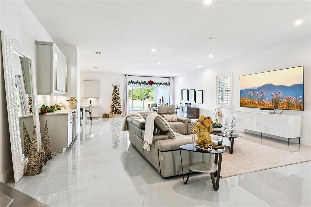 A bright, open-concept living room features light tile floors, a large television, and neutral furniture — 13265 BROMBOROUGH DRIVE, ORLANDO, FL