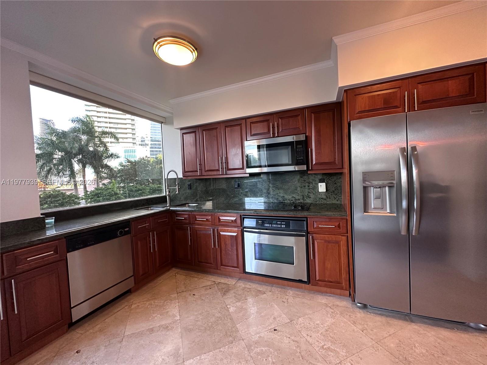 A kitchen features cherry wood cabinets, stainless steel appliances, dark countertops, and a large window — 1541 Brickell Ave # B403, Miami FL 33129, MIAMI, FL