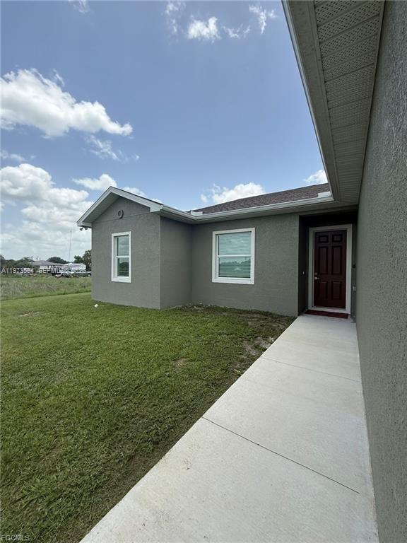 A concrete walkway leads to the red front door of a gray stucco house — 1818 Inwood RD, La Belle FL 33935, LA BELLE, FL