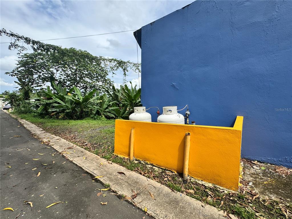 Two propane tanks sit behind a yellow concrete wall next to a blue building — 842 N CAMINO LOS MURIELES, SAN JUAN, PR