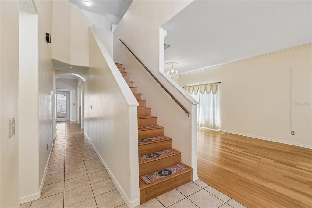 A staircase with patterned treads leads upward beside a tiled hallway and hardwood living area — 12803 LONGCREST DRIVE, RIVERVIEW, FL