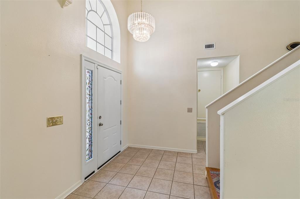 A tiled entryway features a high ceiling, a crystal chandelier, and a white front door — 12803 LONGCREST DRIVE, RIVERVIEW, FL