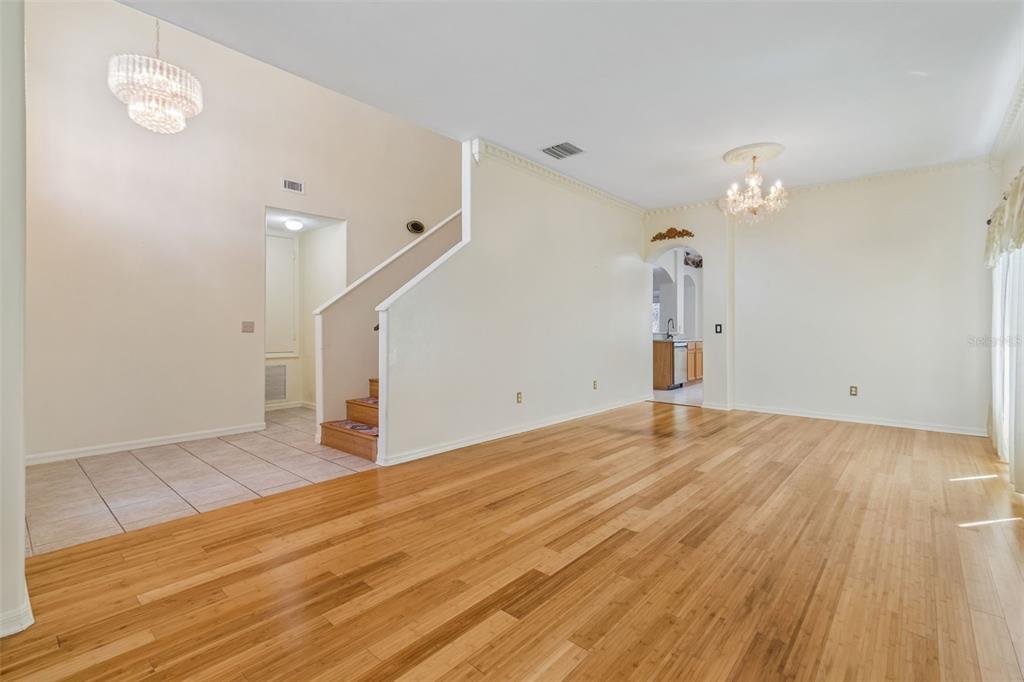 An open living area features light wood flooring, a staircase, and two crystal chandeliers — 12803 LONGCREST DRIVE, RIVERVIEW, FL