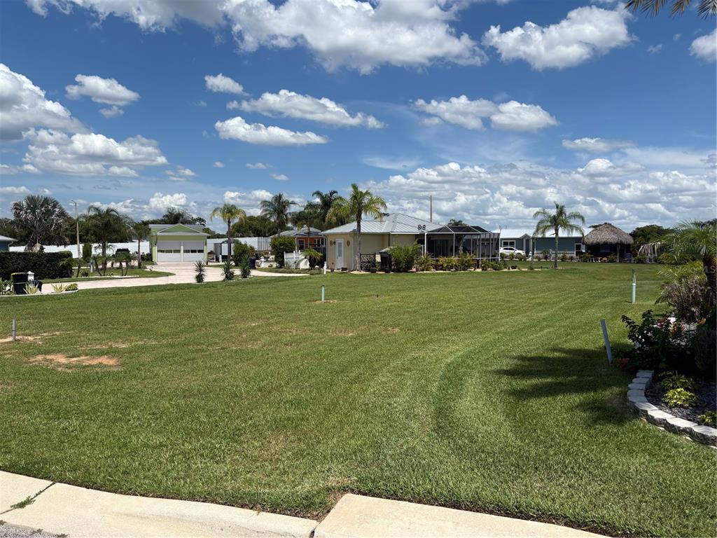 A large, grassy vacant lot sits in front of several houses and palm trees — 2884 WOOD DUCK DRIVE, POLK CITY, FL