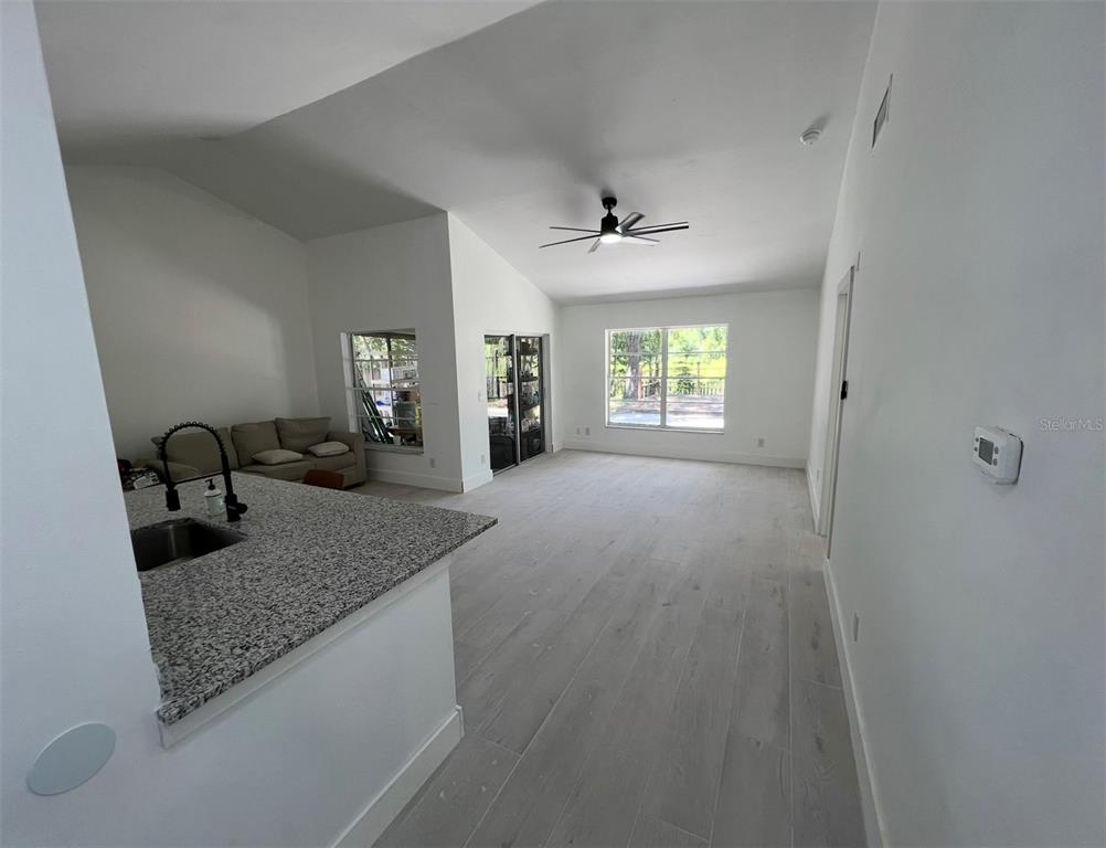 An open-concept living area features light wood-look flooring, a vaulted ceiling, and a granite-topped island — 12824 DUNHILL DRIVE, TAMPA, FL