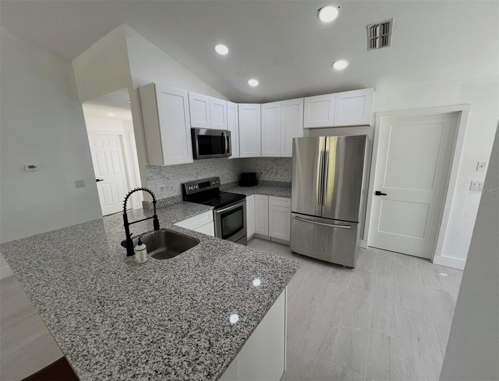 A kitchen features white cabinets, granite countertops, stainless steel appliances, and light-colored tile flooring — 12824 DUNHILL DRIVE, TAMPA, FL