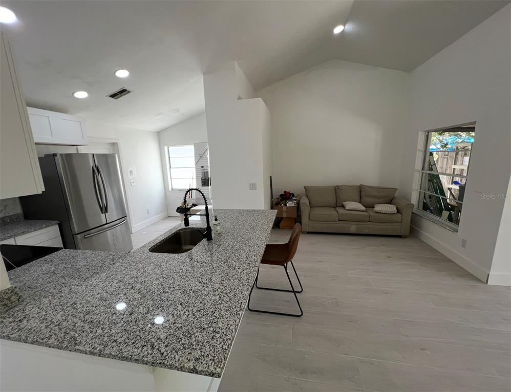 A kitchen with granite countertops and stainless steel appliances opens into a living area — 12824 DUNHILL DRIVE, TAMPA, FL