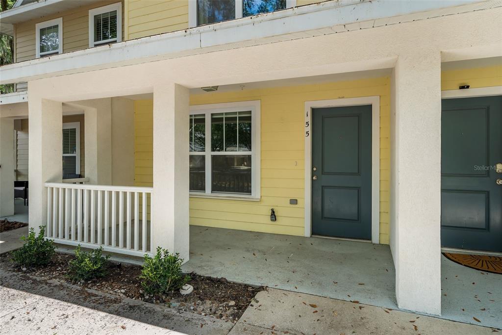 A yellow townhome exterior features a covered porch, a white railing, and a dark door — 4605 SW 48TH DRIVE UNIT 155, GAINESVILLE, FL