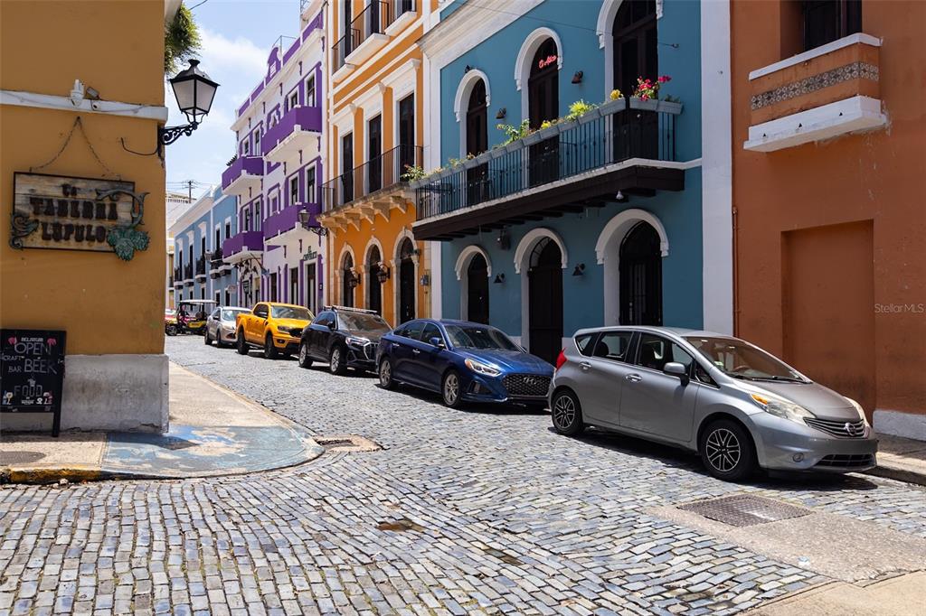 A cobblestone street lined with colorful historic buildings and parked cars in Old San Juan — 9 CALLE DEL MERCADO, SAN JUAN, PR
