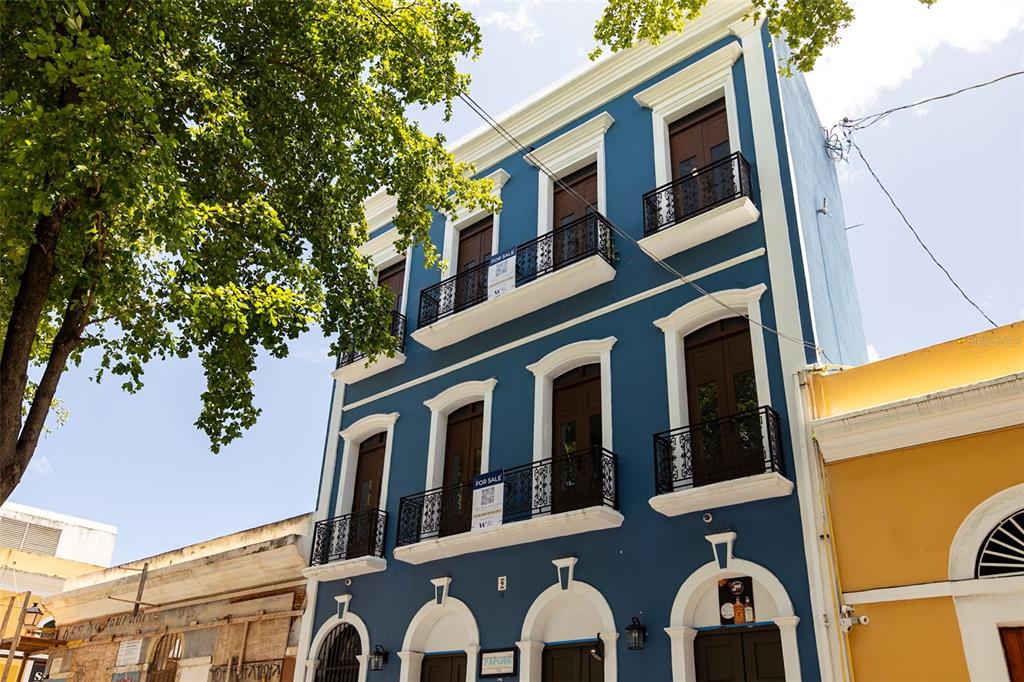 A three-story blue building with arched doorways, balconies, and white trim stands on a street — 9 CALLE DEL MERCADO, SAN JUAN, PR