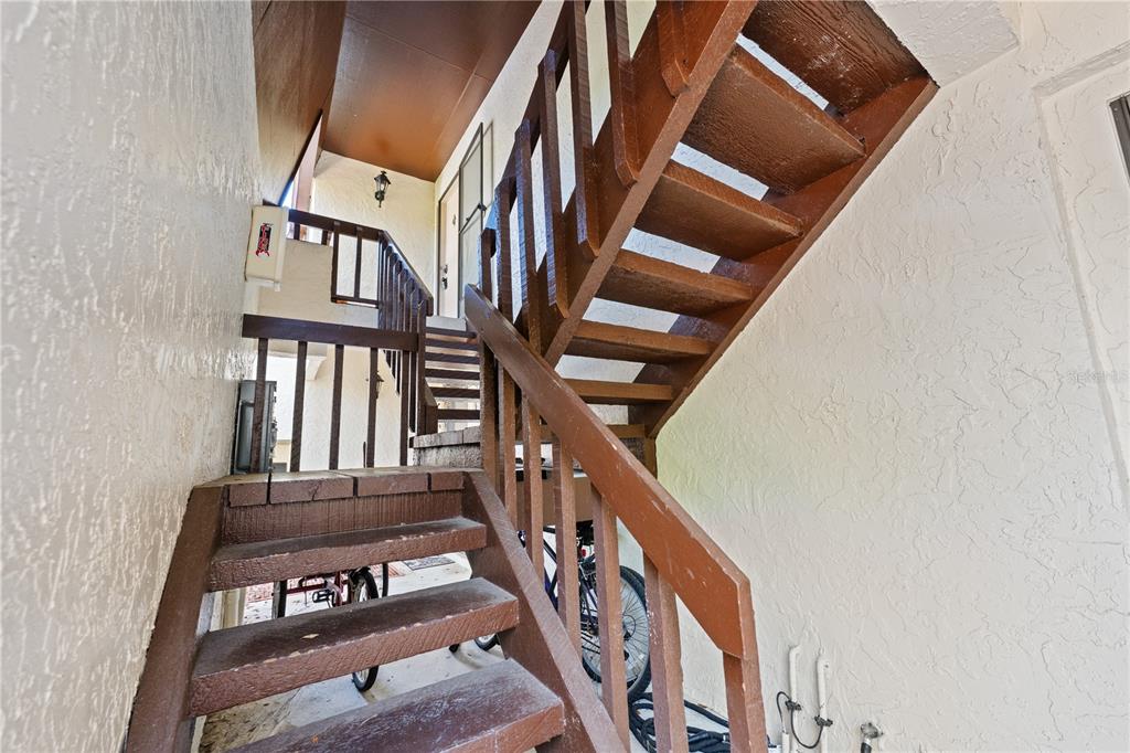 An outdoor wooden staircase leads to an upper-level balcony with a white stucco wall — 4574 RINGWOOD MEADOW UNIT 4, SARASOTA, FL