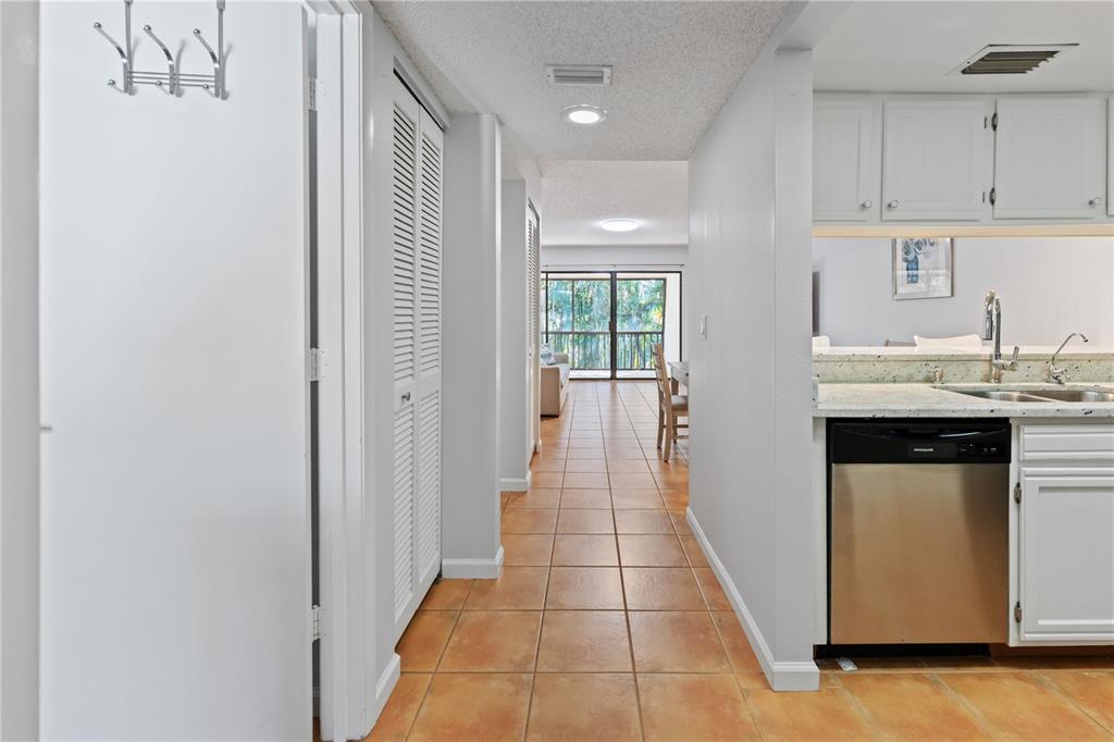 A hallway with tile flooring leads from a kitchen toward a balcony with greenery — 4574 RINGWOOD MEADOW UNIT 4, SARASOTA, FL
