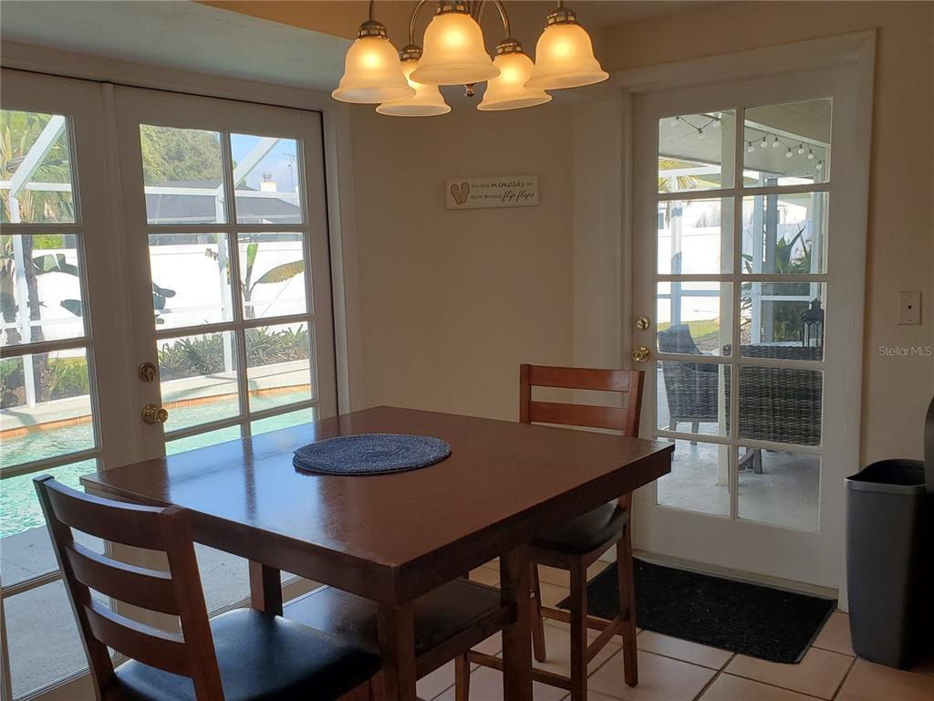 A dining area features a wooden table, chairs, a chandelier, and glass doors to a pool — 2745 CARDWELL WAY, SARASOTA, FL