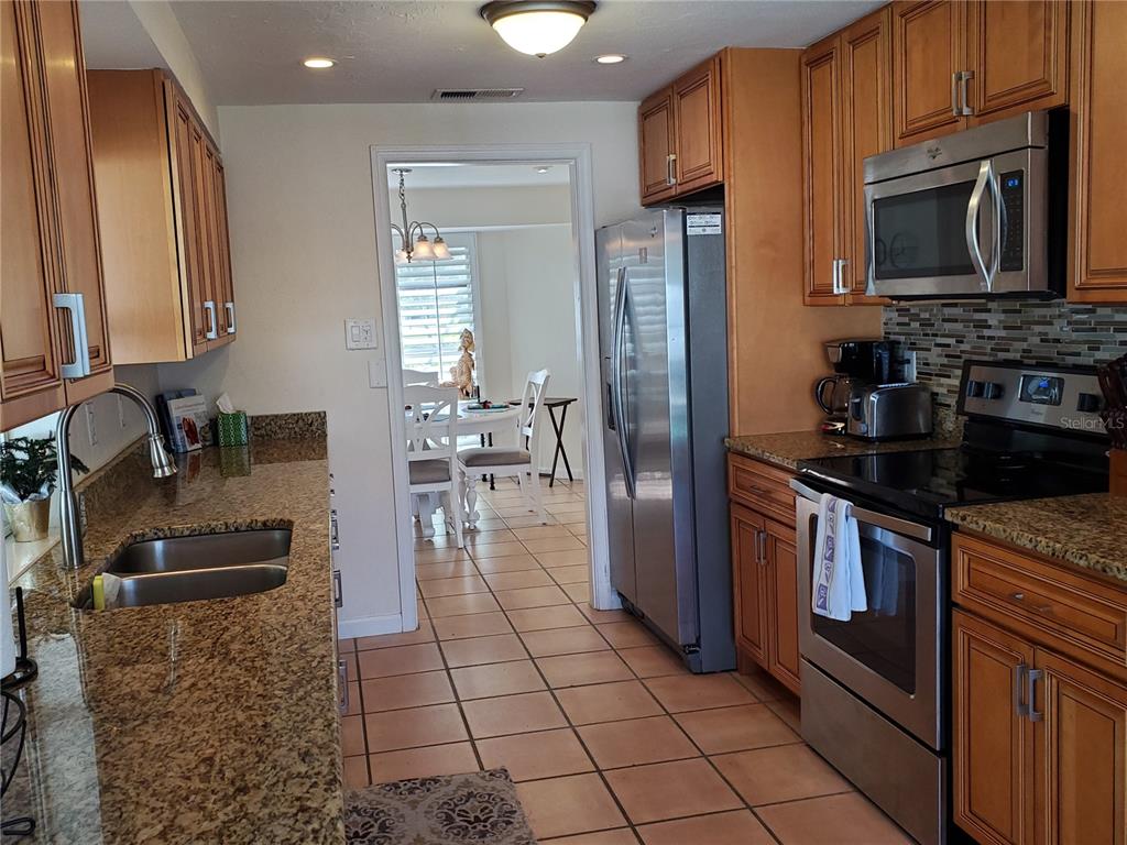 A kitchen with wood cabinets, granite countertops, stainless steel appliances, and tile flooring — 2745 CARDWELL WAY, SARASOTA, FL