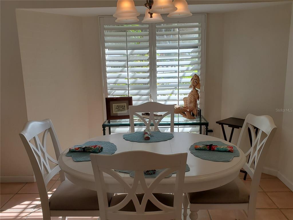 A dining area features a white round table, four chairs, and plantation shutters on the window — 2745 CARDWELL WAY, SARASOTA, FL