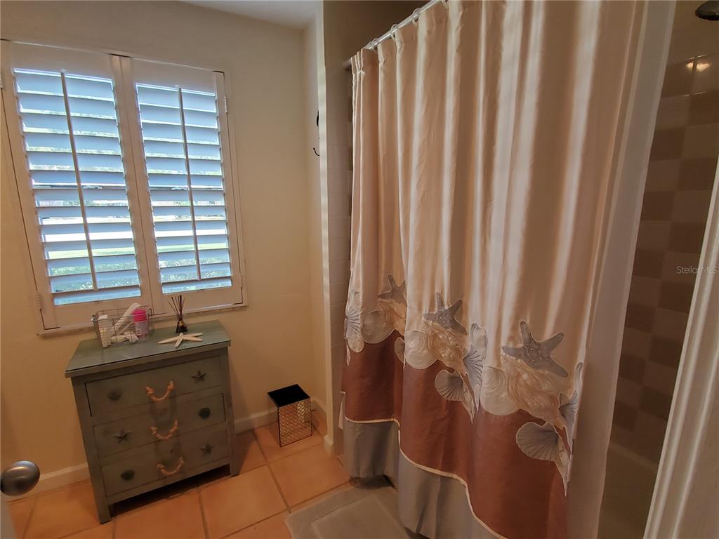 A bathroom features a green dresser, plantation shutters, and a coastal-themed shower curtain — 2745 CARDWELL WAY, SARASOTA, FL