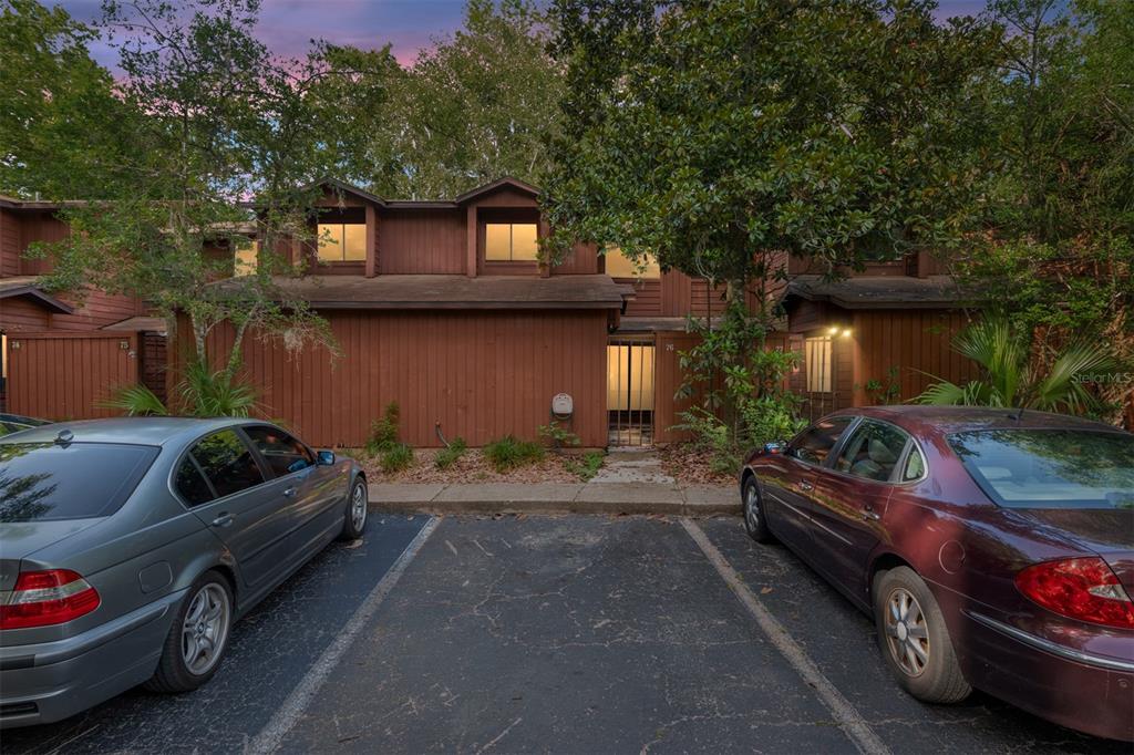 A two-story brown wood-sided townhouse exterior with two parked cars in the foreground — 900 SW 62ND BOULEVARD UNIT L76, GAINESVILLE, FL