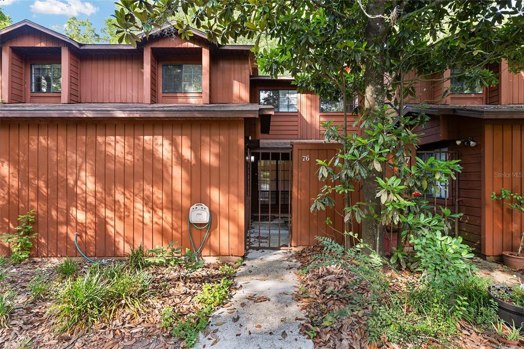The exterior of a brown wood-sided townhouse features a gated entryway and second-story windows — 900 SW 62ND BOULEVARD UNIT L76, GAINESVILLE, FL