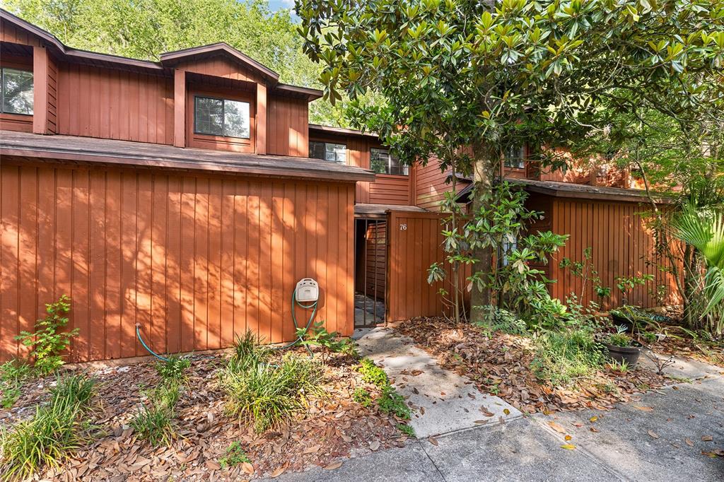 A two-story brown wood-sided townhouse with a gated entryway and a concrete walkway — 900 SW 62ND BOULEVARD UNIT L76, GAINESVILLE, FL