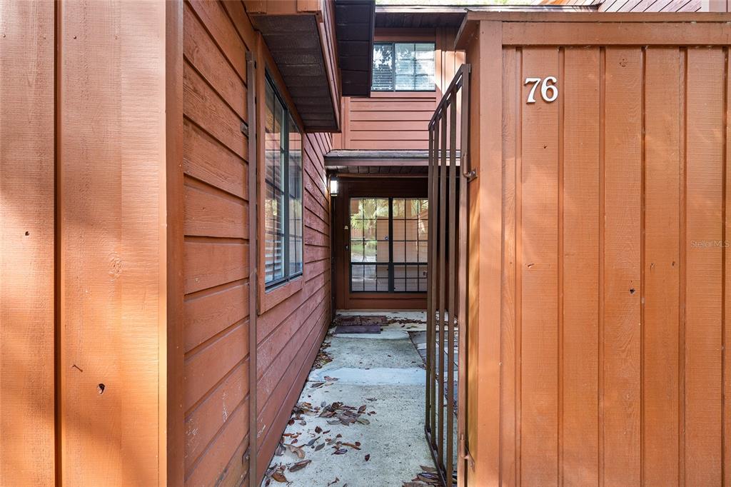 A walkway leads to the entrance of a brown wood-sided home numbered 76 — 900 SW 62ND BOULEVARD UNIT L76, GAINESVILLE, FL