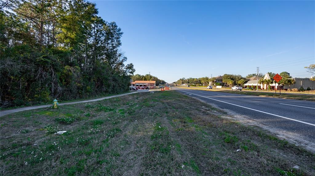 A grassy roadside lot sits next to a paved highway with trees and buildings nearby — 4164 W GULF TO LAKE HIGHWAY, LECANTO, FL
