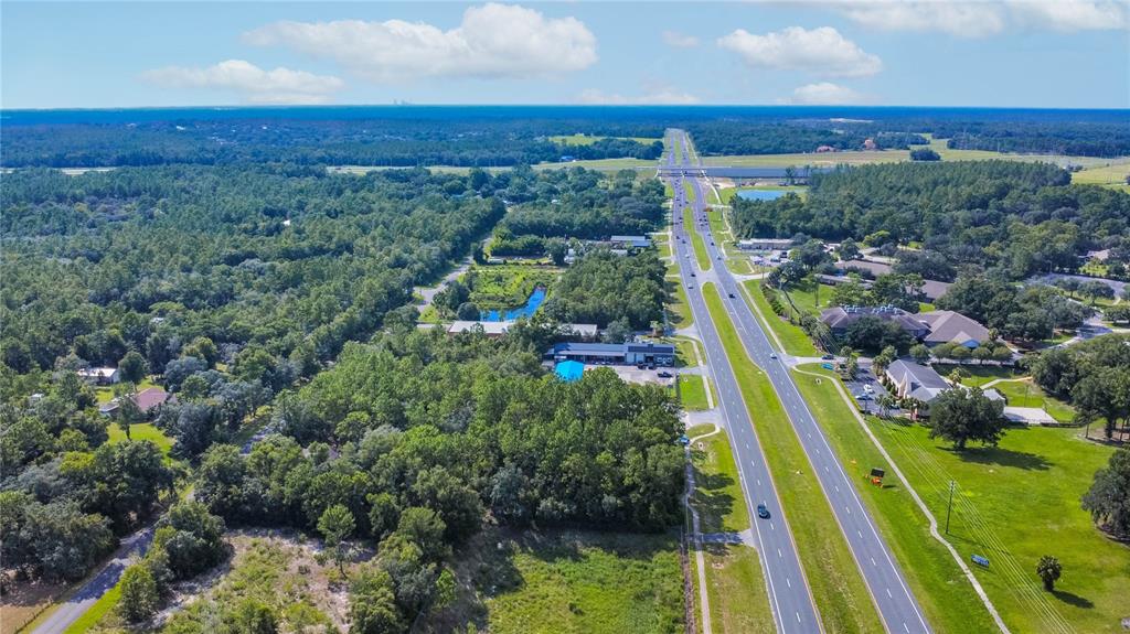 An aerial view shows a multi-lane highway running through a forested area with nearby buildings — 4164 W GULF TO LAKE HIGHWAY, LECANTO, FL