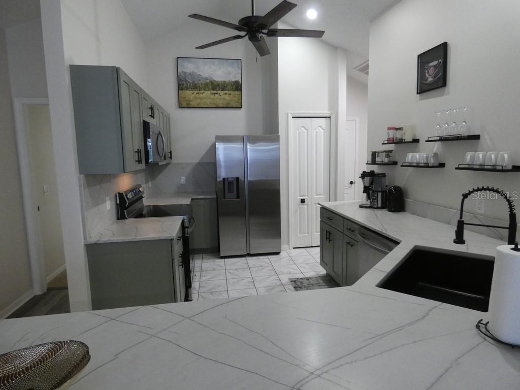 A kitchen features gray cabinets, white marble-look countertops, stainless steel appliances, and a ceiling fan — 6534 FOXMOOR DRIVE, ZEPHYRHILLS, FL