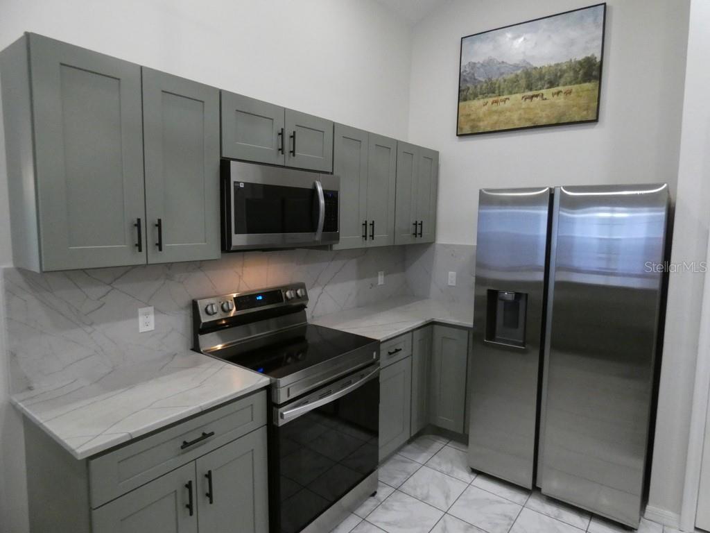 A kitchen features gray cabinets, stainless steel appliances, and white marble-patterned countertops and backsplash — 6534 FOXMOOR DRIVE, ZEPHYRHILLS, FL