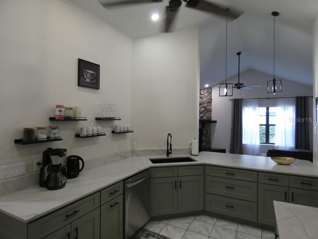 A kitchen with green cabinets, white marble countertops, a corner sink, and floating wall shelves — 6534 FOXMOOR DRIVE, ZEPHYRHILLS, FL
