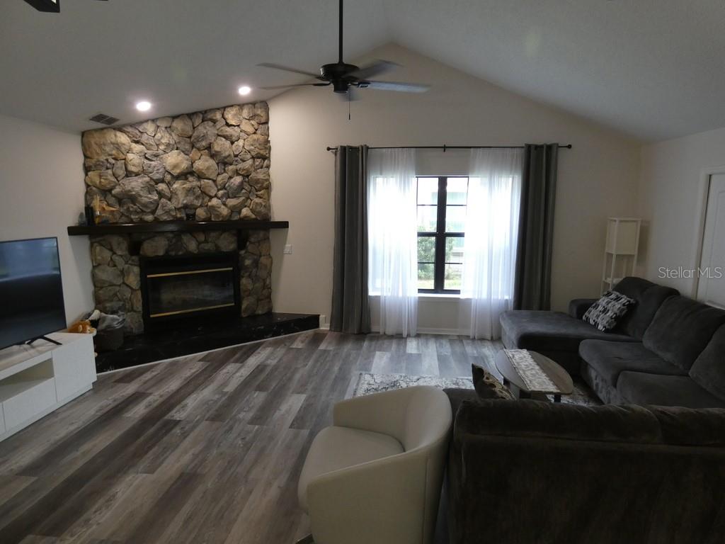 A living room features a stone fireplace, vaulted ceiling, and wood-look flooring — 6534 FOXMOOR DRIVE, ZEPHYRHILLS, FL