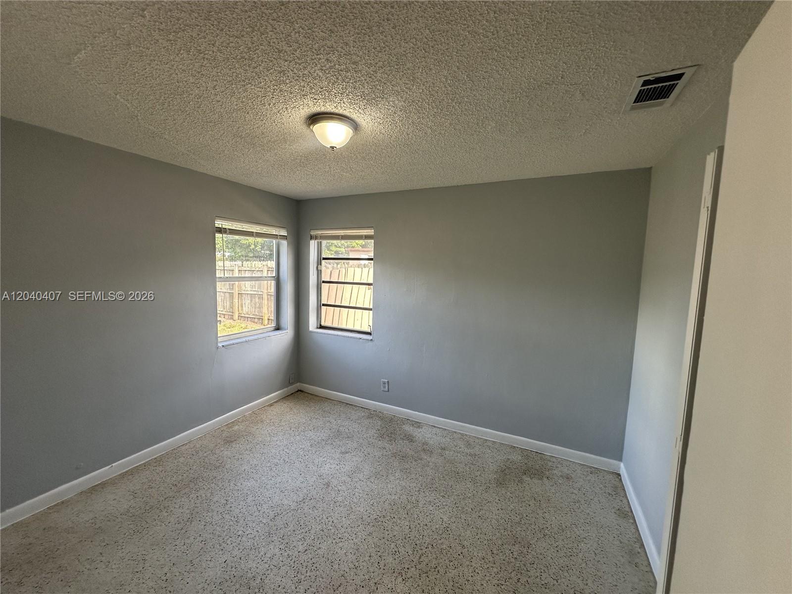 An empty bedroom features gray walls, a popcorn ceiling, two windows, and carpeted flooring — 820 NW 4th Ave, Fort Lauderdale FL 33311, FORT LAUDERDALE, FL